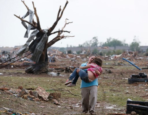 A woman carries her child through a field near the collapsed Plaza Towers Elementary School in Moore, Okla., May 20, 2013.