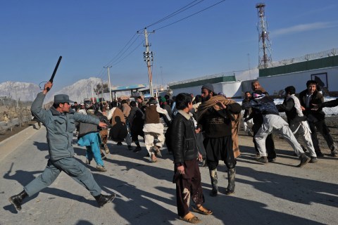An Afghan policeman uses his baton to di