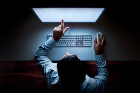 Man points at glowing computer screen in darkness