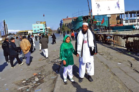 image: Thirteen year old Afghan girl Tarana Akbari walks with her father, Ahmad Shah as they wait to proceed at a police checkpost on the day of Ashura in Kabul, Nov. 24, 2012.