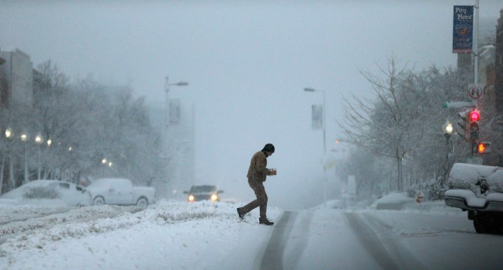 An unidentified man carries coffee to his vehicle across an unplowed street in Lawrence, Kan.