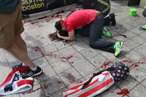 A man comforts a victim on the sidewalk at the scene of the first explosion near the finish line of the 117th Boston Marathon, April 15, 2013.