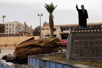 File photo of a man raising his hand as he stands on the spot where the statue of Hafez Al-Assad used to be in Raqqa province
