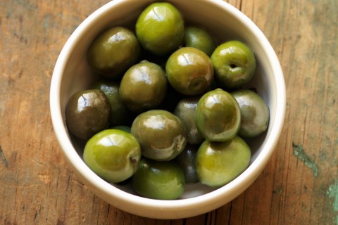 Bowl of gourmet olives on rustic wooden table, close-up