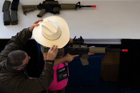 A man adjusts a girl's hat before she takes aim with an airsoft gun during the NRA Youth Day at the National Rifle Association's annual meeting in Houston, Texas