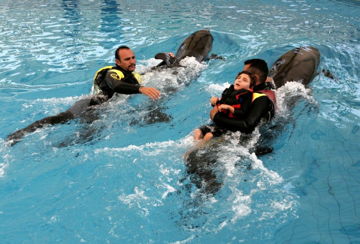From left: Divers Murat Cicek and Yusuf Yurdasiper hold on to fins of dolphins swim to assist a three-year-old Turkish girl Ayse suffering from cerebral palsy during a therapy session in Antalya, Turkey, on  June 12, 2005. Children suffering autism or cerebral palsy are treated under the supervision of Dr. Murat Kemaloglu with the help of Cicek  and Yurdasiper, both divers and pedagogues.