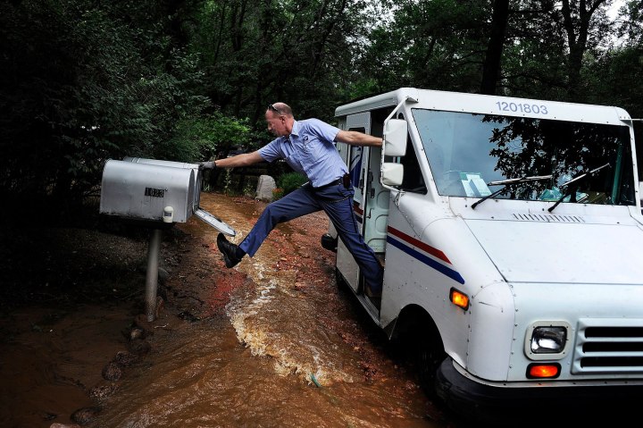 Dave Jackson closes a mailbox with his foot after delivering the mail to a home surrounded on three sides by a flooded Cheyenne Creek in Colorado Springs, Colo., Sept. 13, 2013.