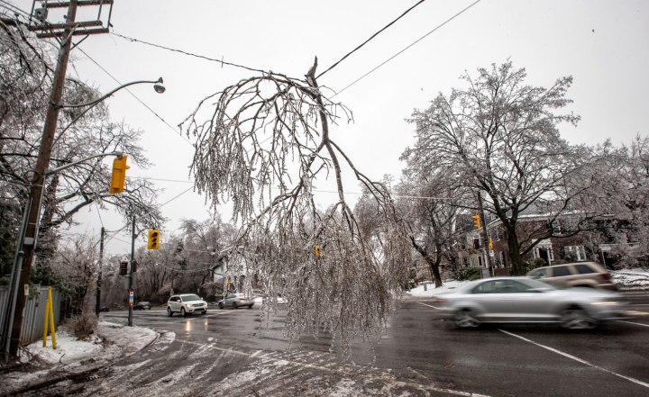 Cars drive by a fallen tree limb hanging from a power line following an ice storm in Toronto, on Dec. 22, 2013.