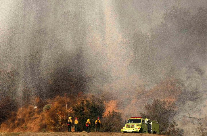 Firefighters stand as water falls from a firefighting aircraft on the Colby Fire in Azusa, California