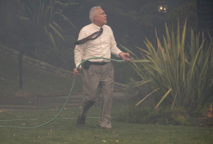A local resident uses a garden hose to protect his home from a fast-moving California wildfire, so-called the "Colby Fire", in the hills of Glendora