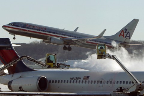 A Delta jetliner is de-iced while an American Airlines plane takes off at Reagan National Airport in Washington