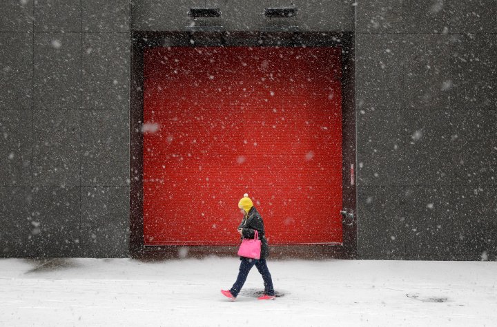 A woman walks outside of an office building as snow falls, Jan. 21, 2014, in Baltimore. 